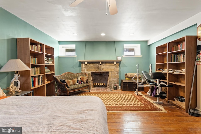 bedroom with ceiling fan, a stone fireplace, and hardwood / wood-style floors