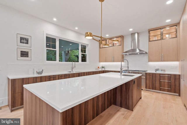 kitchen featuring tasteful backsplash, an island with sink, modern cabinets, wall chimney exhaust hood, and a sink