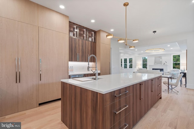 kitchen featuring a tray ceiling, backsplash, a center island with sink, pendant lighting, and light wood-type flooring