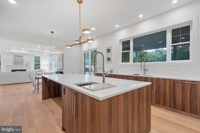 kitchen with a healthy amount of sunlight, a kitchen island with sink, pendant lighting, light hardwood / wood-style floors, and sink