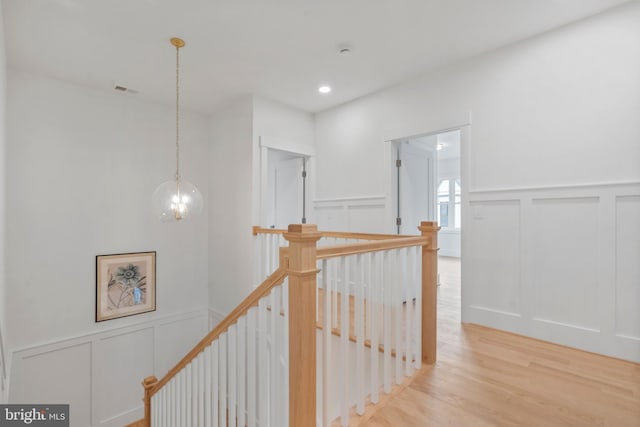 corridor featuring an upstairs landing, recessed lighting, a decorative wall, an inviting chandelier, and light wood finished floors