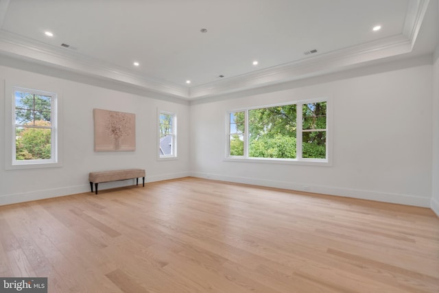 spare room with a tray ceiling, light wood-style floors, baseboards, and ornamental molding