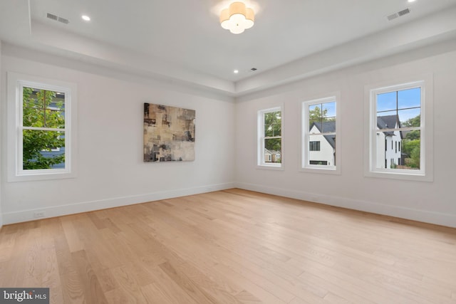 empty room with light wood-type flooring, visible vents, and a raised ceiling