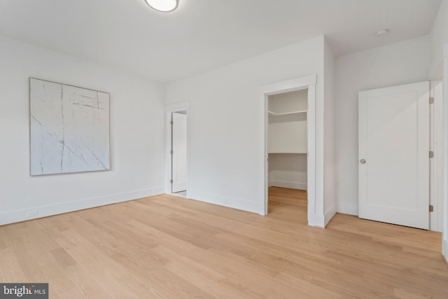 unfurnished bedroom with a walk in closet, baseboards, a closet, and light wood-style flooring