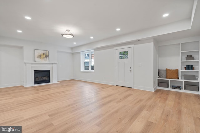 unfurnished living room featuring recessed lighting, a glass covered fireplace, light wood-style flooring, and baseboards