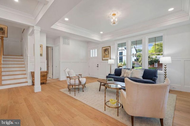 living room with a raised ceiling, ornamental molding, and light hardwood / wood-style flooring