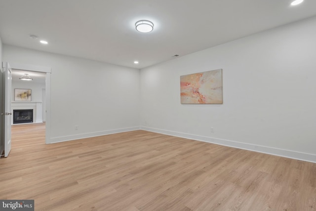 empty room featuring a glass covered fireplace, light wood-style flooring, recessed lighting, and baseboards