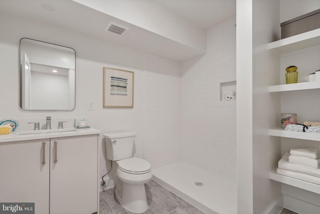 full bathroom with vanity, wood finished floors, visible vents, tiled shower, and toilet