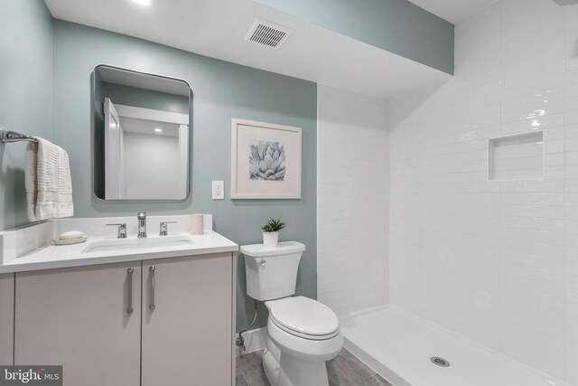 full bath featuring vanity, wood finished floors, visible vents, tiled shower, and toilet