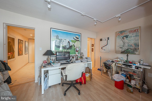 office space with built in desk, track lighting, a textured ceiling, and light wood-type flooring