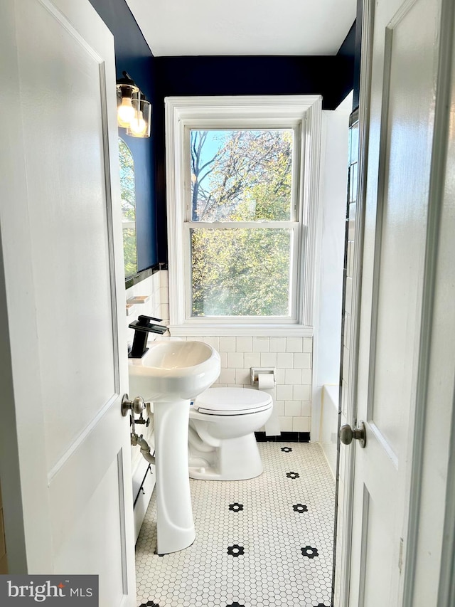 bathroom with tile walls, tile patterned flooring, a washtub, and toilet