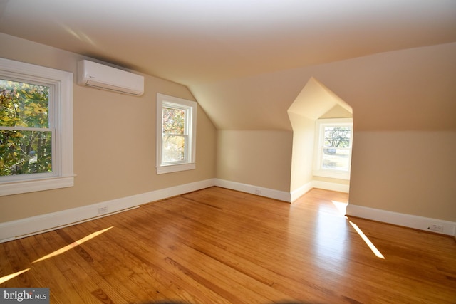 additional living space with an AC wall unit, vaulted ceiling, and light wood-type flooring