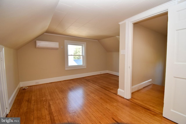 bonus room with vaulted ceiling, a wall unit AC, and light wood-type flooring