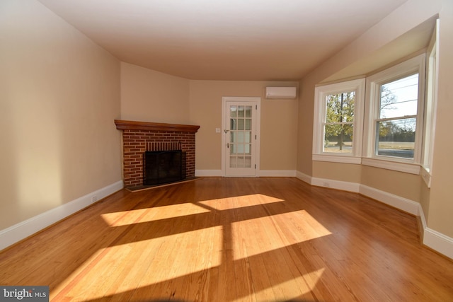 unfurnished living room featuring hardwood / wood-style floors, a wall mounted AC, and a brick fireplace