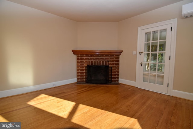 unfurnished living room featuring a wall unit AC, hardwood / wood-style flooring, and a brick fireplace