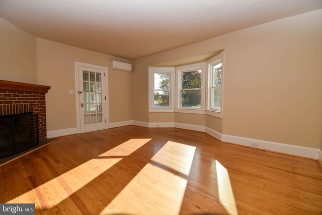 unfurnished living room with a wall mounted AC, wood-type flooring, and a fireplace