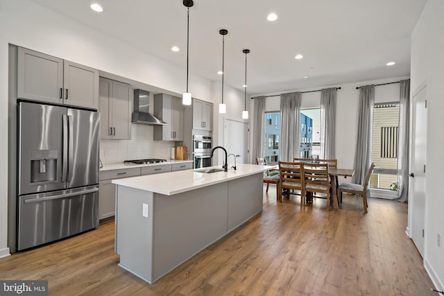 kitchen featuring wall chimney range hood, appliances with stainless steel finishes, gray cabinetry, and hanging light fixtures