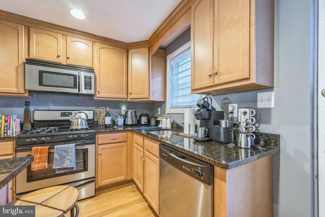 kitchen with dark stone countertops, sink, appliances with stainless steel finishes, and light hardwood / wood-style flooring