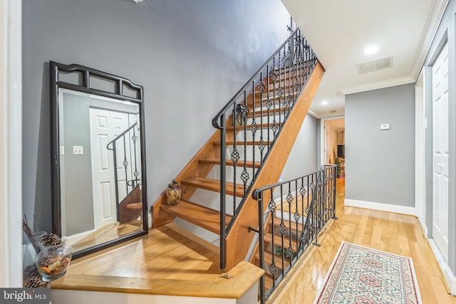 stairway with wood-type flooring and ornamental molding