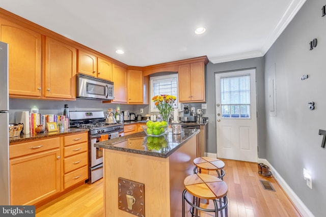 kitchen with dark stone countertops, crown molding, light hardwood / wood-style floors, a kitchen island, and appliances with stainless steel finishes