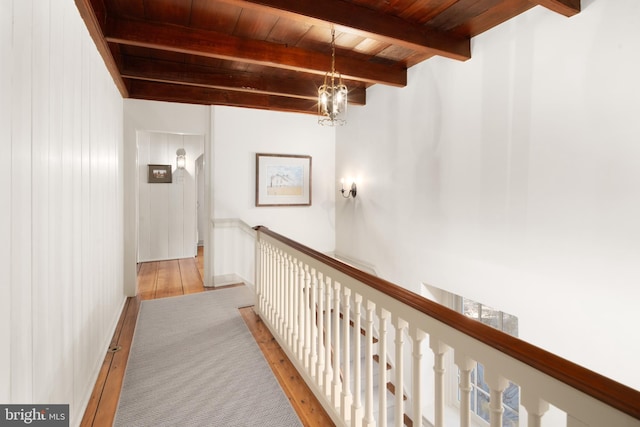 corridor featuring beam ceiling, wood walls, light hardwood / wood-style floors, a chandelier, and wooden ceiling