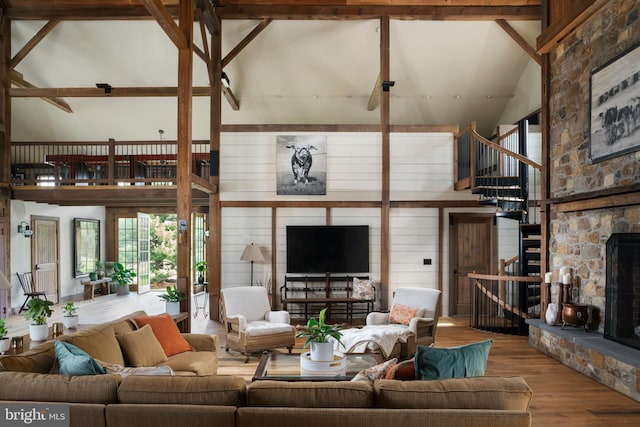 living room with a stone fireplace, beam ceiling, high vaulted ceiling, wooden walls, and hardwood / wood-style floors