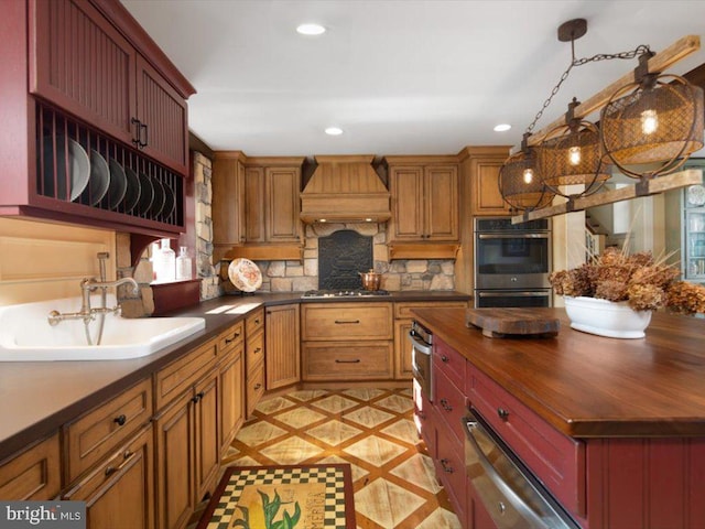 kitchen with backsplash, appliances with stainless steel finishes, hanging light fixtures, sink, and custom exhaust hood