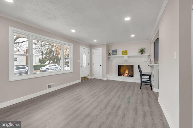 unfurnished living room featuring a fireplace, a textured ceiling, light wood-type flooring, and ornamental molding