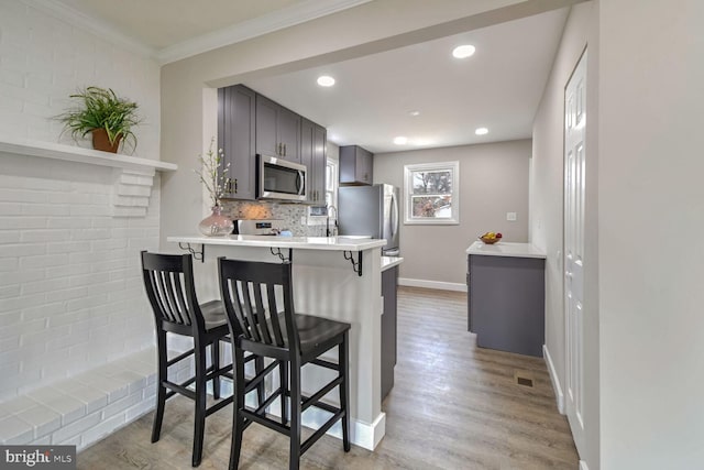 kitchen with stainless steel appliances, backsplash, kitchen peninsula, a kitchen bar, and light wood-type flooring