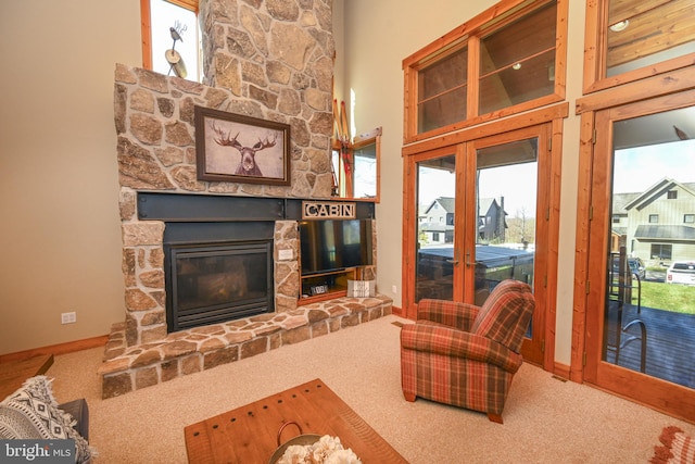 living room with french doors, a towering ceiling, a stone fireplace, and carpet flooring