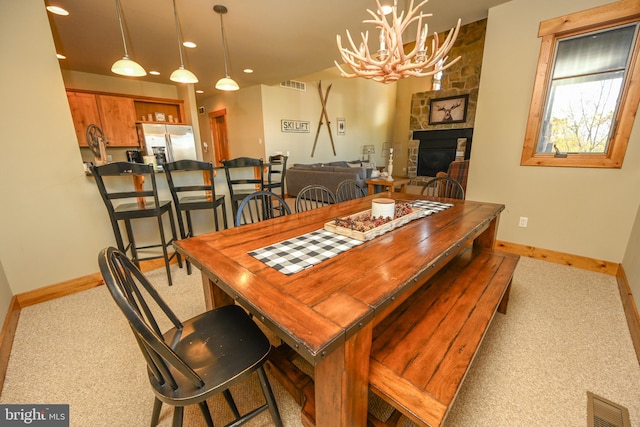 dining room with a chandelier, a stone fireplace, and light colored carpet