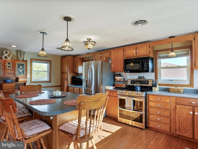 kitchen featuring appliances with stainless steel finishes, backsplash, a breakfast bar area, hanging light fixtures, and light hardwood / wood-style flooring