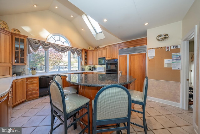 kitchen with dark stone counters, light tile patterned flooring, black appliances, a skylight, and a center island