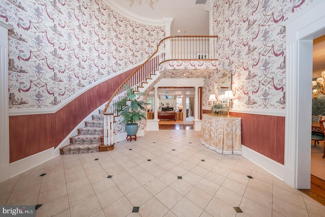 tiled entryway with ornate columns, crown molding, and a high ceiling