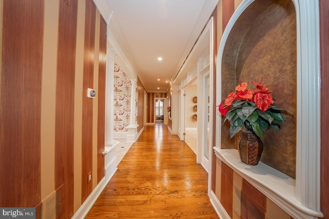 hall featuring ornate columns, crown molding, and light wood-type flooring