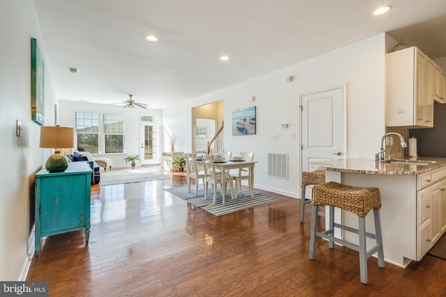 kitchen featuring light stone countertops, sink, dark hardwood / wood-style flooring, ceiling fan, and a breakfast bar