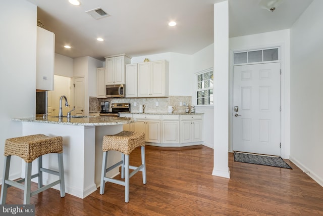 kitchen featuring decorative backsplash, dark hardwood / wood-style floors, kitchen peninsula, stainless steel appliances, and light stone countertops