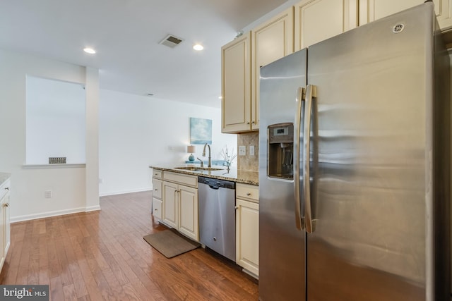 kitchen with cream cabinets, wood-type flooring, sink, light stone countertops, and appliances with stainless steel finishes