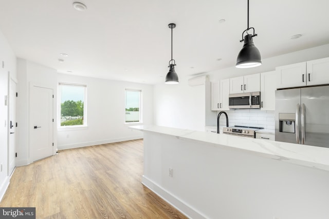 kitchen featuring stainless steel appliances, light stone countertops, pendant lighting, light wood-type flooring, and white cabinets