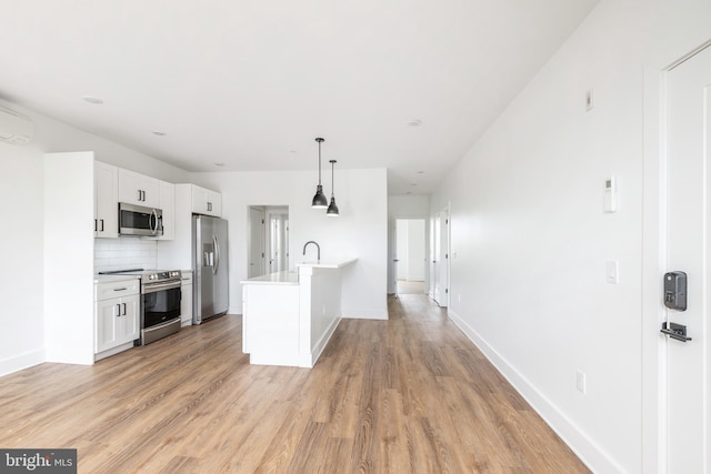 kitchen featuring decorative backsplash, stainless steel appliances, pendant lighting, white cabinetry, and light hardwood / wood-style floors