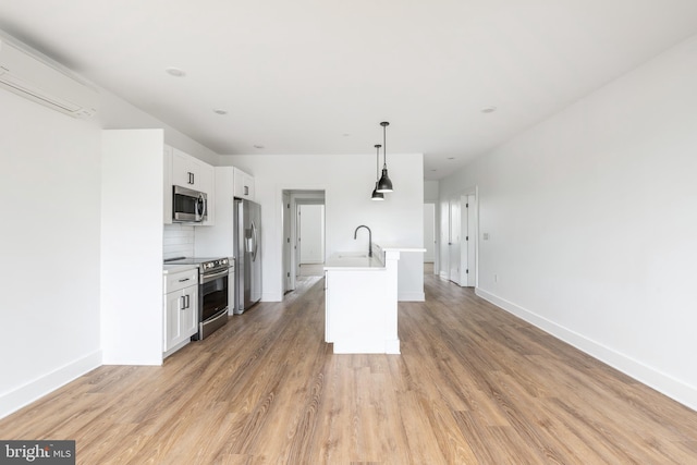 kitchen with stainless steel appliances, pendant lighting, white cabinets, light hardwood / wood-style flooring, and a kitchen island with sink