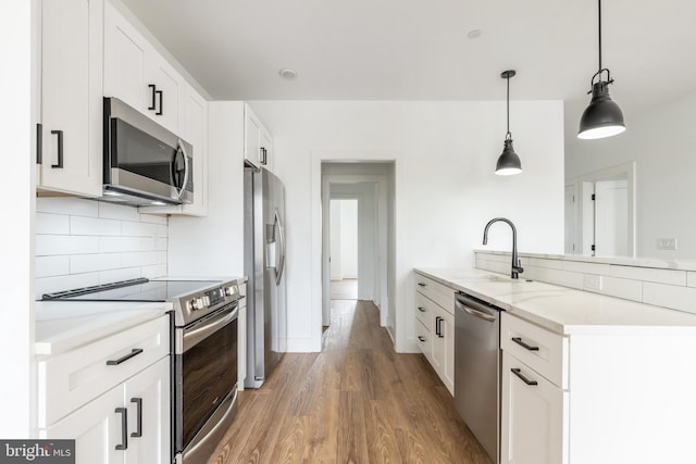 kitchen featuring hardwood / wood-style floors, hanging light fixtures, white cabinetry, sink, and stainless steel appliances