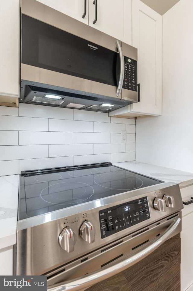 interior details with appliances with stainless steel finishes, white cabinetry, and tasteful backsplash