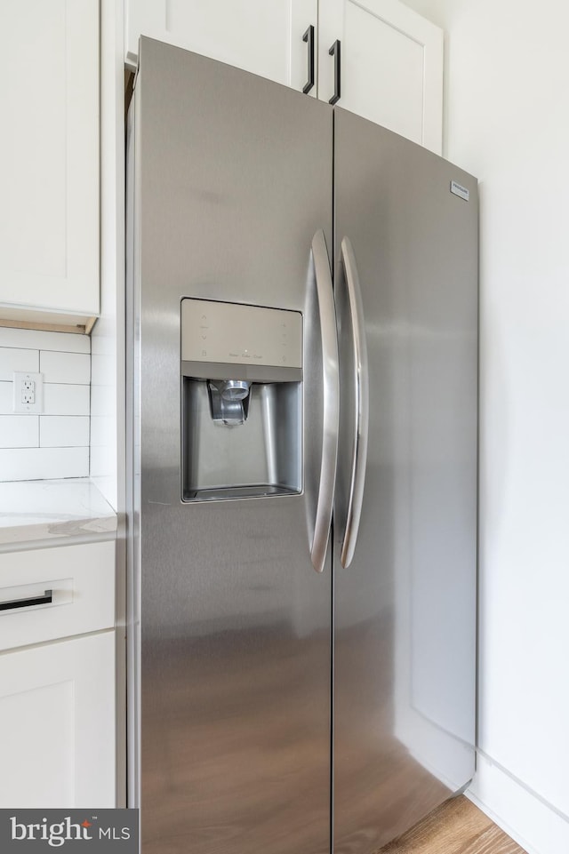 room details with decorative backsplash, light hardwood / wood-style flooring, stainless steel fridge, light stone countertops, and white cabinetry