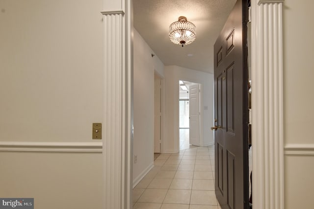 hallway featuring an inviting chandelier, a textured ceiling, and light tile patterned floors