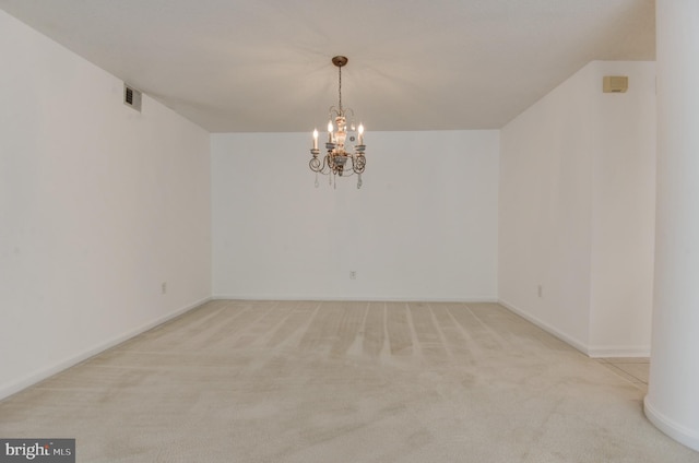 spare room featuring a chandelier and light colored carpet