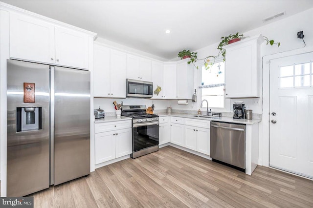 kitchen featuring appliances with stainless steel finishes, white cabinetry, a healthy amount of sunlight, and light wood-type flooring