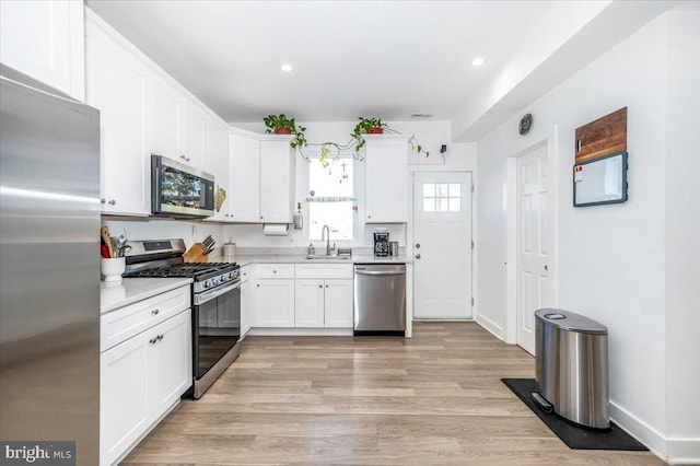 kitchen with sink, appliances with stainless steel finishes, light hardwood / wood-style floors, and white cabinets