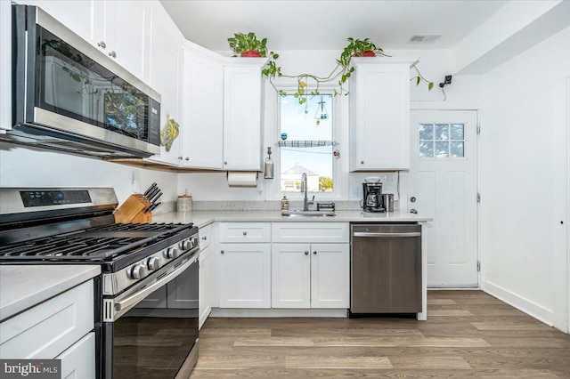 kitchen with sink, white cabinets, light hardwood / wood-style flooring, and stainless steel appliances