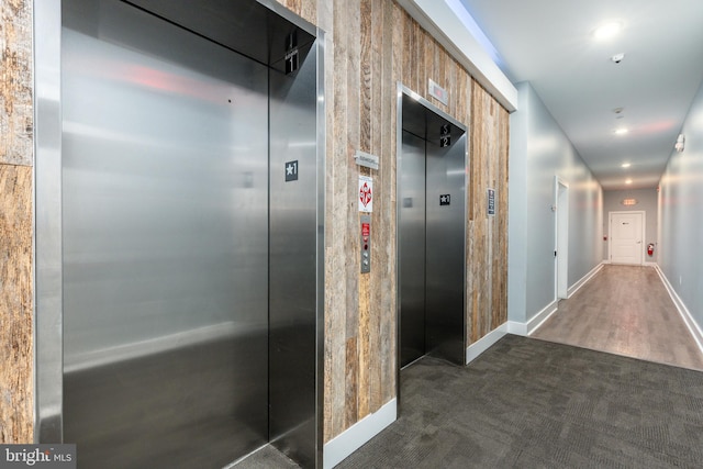 hallway with elevator and dark colored carpet